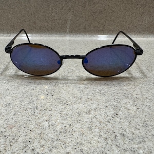 May include: Oval-shaped sunglasses featuring a thin black metal frame and dark lenses with a distinct blue and purple reflective tint. The eyewear has slender temples and a simple bridge connecting the two oval lenses, creating a sleek look.