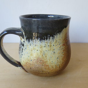 May include: A ceramic mug with a black, white, and brown glaze. The mug has a rounded body and a handle.