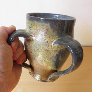 May include: A ceramic mug with two handles, featuring a speckled brown, gray, and gold glaze.
