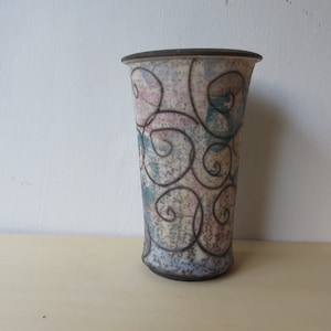 May include: A ceramic vase with a white background and a black swirl design. The vase has a light pink and blue glaze.