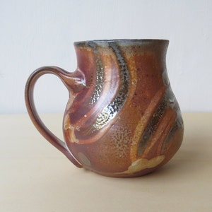 May include: A brown ceramic mug with a wide base and a handle. The mug has a swirling pattern of brown, orange, and white glaze.