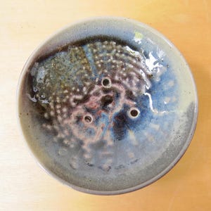 May include: A ceramic dish with a blue, green and brown glaze. The dish has three holes in the bottom.
