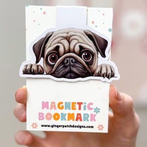 May include: A white magnetic bookmark with a cartoon pug peeking over the top. The bookmark has colorful polka dots and the text "MAGNETIC BOOKMARK" in rainbow colors. The text "www.gingerpatchdesigns.com" is printed below the bookmark.