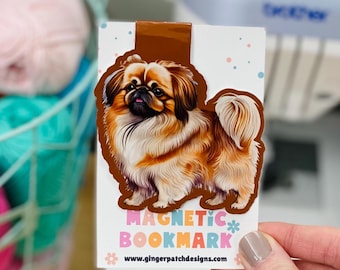 May include: A magnetic bookmark featuring a brown and white Pekingese dog. The bookmark is on a white card with the text "MAGNETIC BOOKMARK" and a website address.