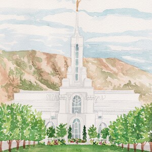 May include: A watercolor painting of a white temple with a golden statue on top. The temple is surrounded by green trees and a grassy lawn. The sky is blue with white clouds. The text "SUZANNE BLAIR designs" is written on the temple.