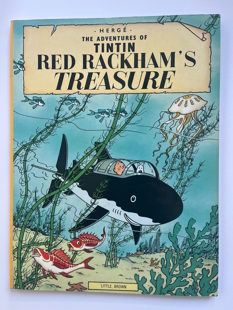 May include: A vintage book cover for "The Adventures of Tintin: Red Rackham's Treasure." The cover features a shark-shaped submarine with Tintin and Snowy inside, surrounded by marine life. The title is in bold red letters.