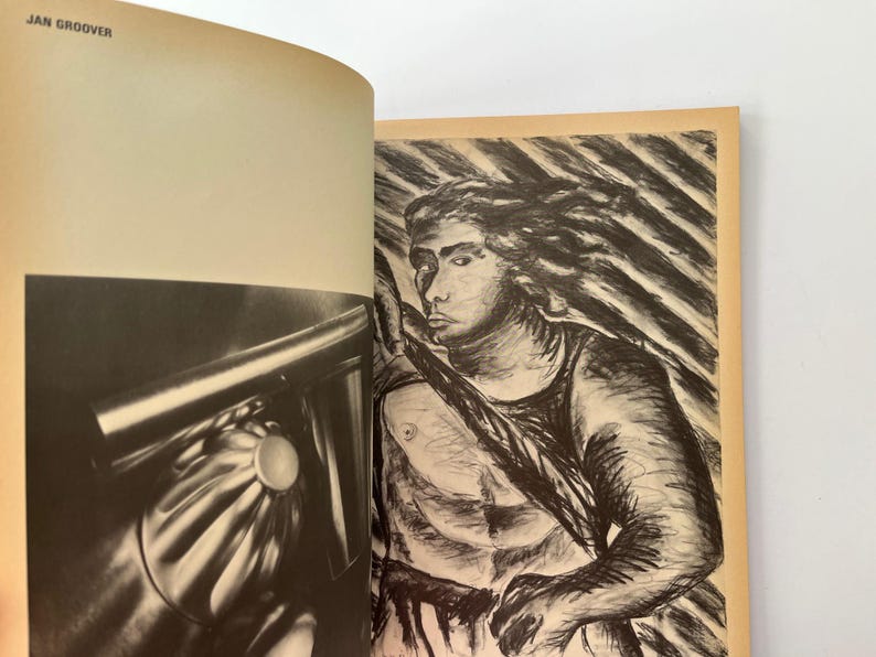 K&ouml;nnte beinhalten: Ein offenes Buch mit zwei Bildern. Die linke Seite zeigt eine Schwarz-Wei&szlig;-Fotografie eines metallischen Objekts mit einem kreisf&ouml;rmigen Element. Die rechte Seite zeigt eine Kohlezeichnung einer Person, die einen Speer h&auml;lt.