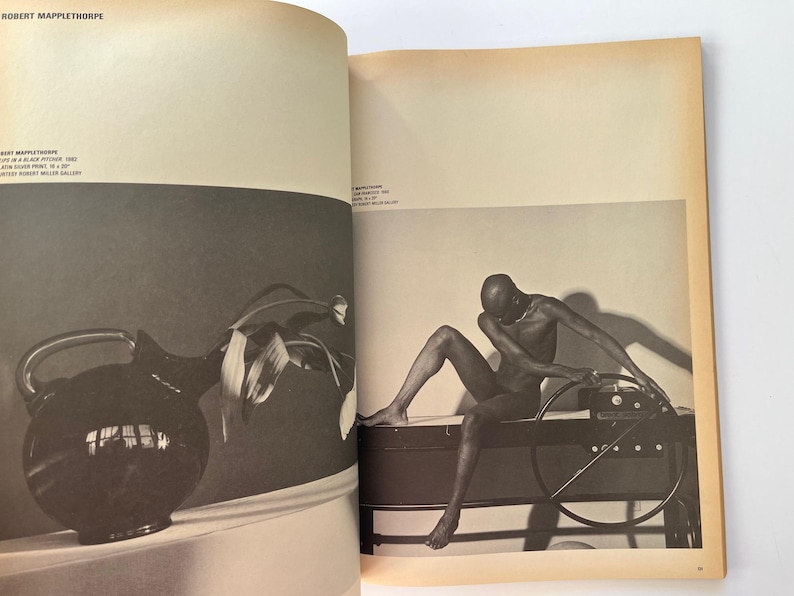 K&ouml;nnte beinhalten: Schwarz-Wei&szlig;-Fotografie aus einem Buch. Links eine dunkle Kanne mit Henkel und Bl&auml;ttern. Rechts sitzt eine nackte Person auf einem dunklen Objekt mit einem kreisf&ouml;rmigen Rad.