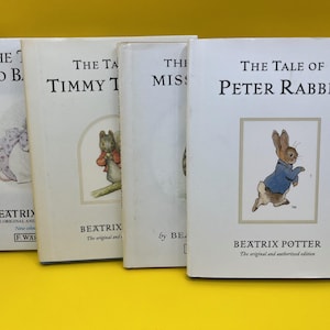 Op de afbeelding: Vier vintage kinderboeken van Beatrix Potter, waaronder "The Tale of Peter Rabbit". De boeken hebben witte covers met illustraties van dieren en tekst. De boeken worden gepresenteerd op een gele ondergrond.
