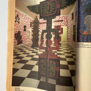 K&ouml;nnte beinhalten: Eine Magazinseite mit einer Kunstinstallation von Keith Haring. Die Installation umfasst gro&szlig;e, farbenfrohe, abstrakte Skulpturen in einem Raum mit einem schwarz-wei&szlig; karierten Boden und W&auml;nden, die mit rot-wei&szlig;en Mustern bedeckt sind.