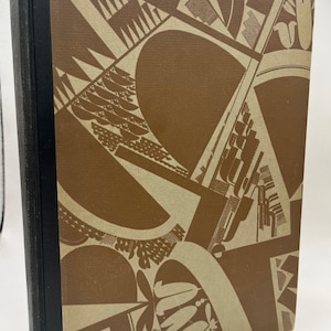 Pode incluir: Um livro de capa dura com uma capa marrom com um design geométrico em um marrom mais claro. A lombada é preta. O livro está em pé, mostrando os padrões intrincados.