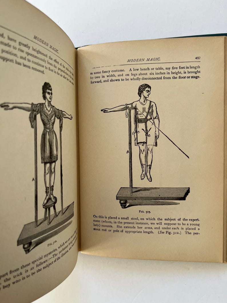 K&ouml;nnte beinhalten: Ein offenes Buch mit Illustrationen aus "Modern Magic". Die Zeichnungen zeigen Figuren, die scheinbar schweben oder Illusionen vollf&uuml;hren. Der Text enth&auml;lt Ma&szlig;e in Fu&szlig; und Zoll sowie Beschreibungen der Tricks.