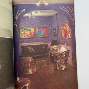 K&ouml;nnte beinhalten: Ein Magazin-Doppelseite mit einem Innenraum mit lila gemusterter Tapete, Kunstwerken und verzierten M&ouml;beln. Der Raum umfasst ein Sofa, zwei St&uuml;hle, einen Tisch und einen Zebra-Print-Teppich. Die Beleuchtungsk&ouml;rper und M&ouml;bel haben eine goldene und verspiegelte Oberfl&auml;che.