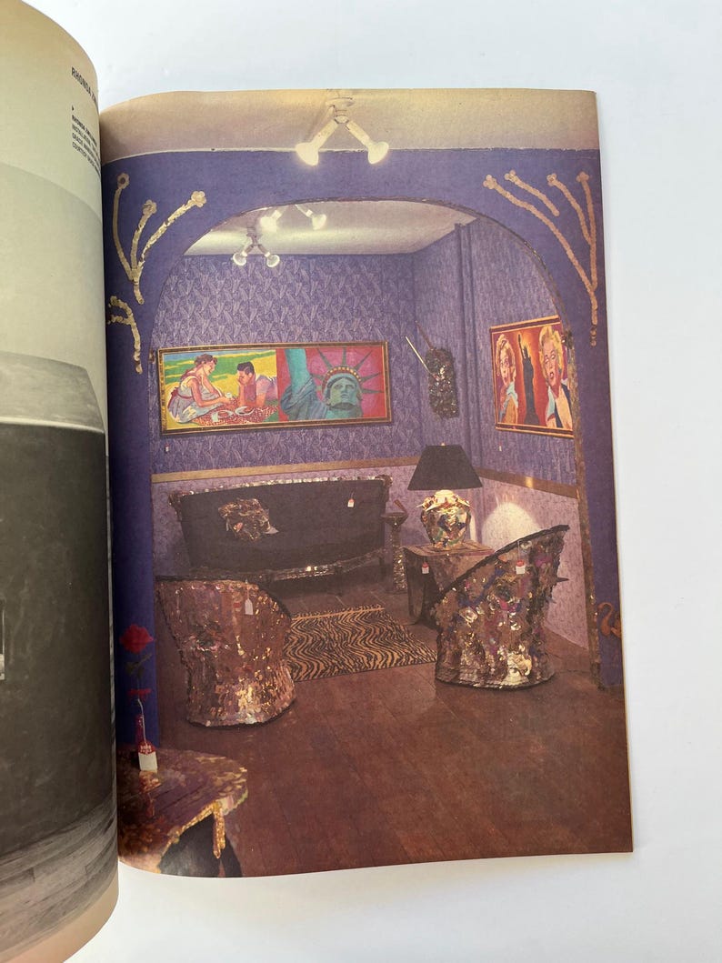 K&ouml;nnte beinhalten: Ein Magazin-Doppelseite mit einem Innenraum mit lila gemusterter Tapete, Kunstwerken und verzierten M&ouml;beln. Der Raum umfasst ein Sofa, zwei St&uuml;hle, einen Tisch und einen Zebra-Print-Teppich. Die Beleuchtungsk&ouml;rper und M&ouml;bel haben eine goldene und verspiegelte Oberfl&auml;che.