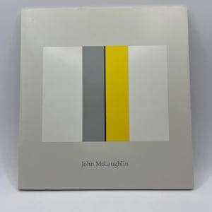 May include: A white card with a black, grey, and yellow geometric design. The text "John McLaughlin" is printed at the bottom of the card.