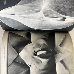 Pode incluir: Uma fotografia a preto e branco de uma escultura geom&eacute;trica. A escultura &eacute; feita de metal e tem um design complexo e abstrato. A escultura &eacute; iluminada de lado, criando um efeito dram&aacute;tico.