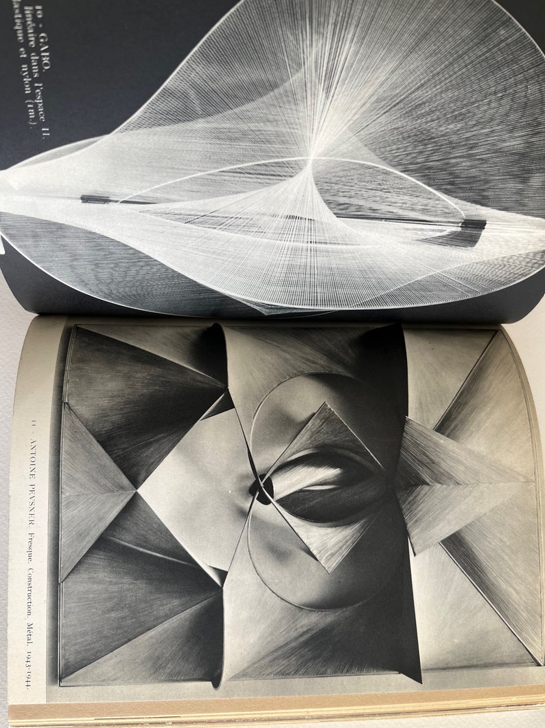Pode incluir: Uma fotografia a preto e branco de uma escultura geom&eacute;trica. A escultura &eacute; feita de metal e tem um design complexo e abstrato. A escultura &eacute; iluminada de lado, criando um efeito dram&aacute;tico.