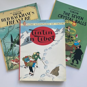 May include: Three vintage Tintin comic books. Titles include "Red Rackham's Treasure", "Tintin in Tibet", and "The Seven Crystal Balls". The covers feature colorful illustrations and text, with a white background.