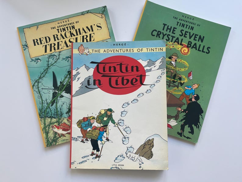 May include: Three vintage Tintin comic books. Titles include "Red Rackham's Treasure", "Tintin in Tibet", and "The Seven Crystal Balls". The covers feature colorful illustrations and text, with a white background.