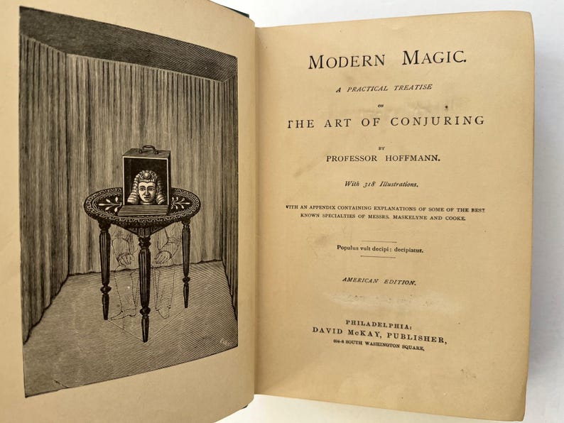 K&ouml;nnte beinhalten: Ein altes Buch mit dem Titel "Modern Magic" und einer Illustration eines Zaubertricks. Die Abbildung zeigt eine Kiste auf einem Tisch mit dem Kopf einer Person darin. Es ist eine amerikanische Ausgabe.