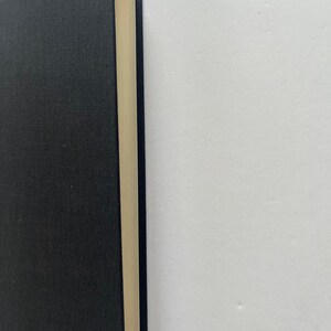 May include: A hardcover book with a black cover and cream-colored pages. The book's spine is visible, showing the edge of the pages. The cover has a textured appearance. The book is set against a white background.