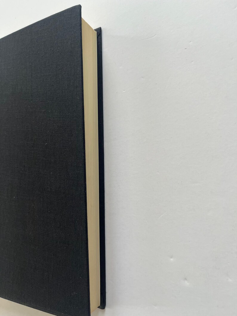 May include: A hardcover book with a black cover and cream-colored pages. The book's spine is visible, showing the edge of the pages. The cover has a textured appearance. The book is set against a white background.