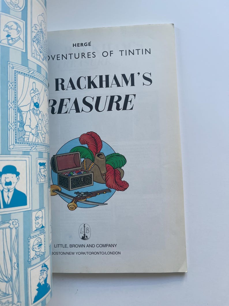 May include: A vintage copy of "The Adventures of Tintin: Red Rackham's Treasure" by Herg&eacute;. The cover features a colorful illustration of a treasure chest, feathers, and a pistol. The book is published by Little, Brown and Company.
