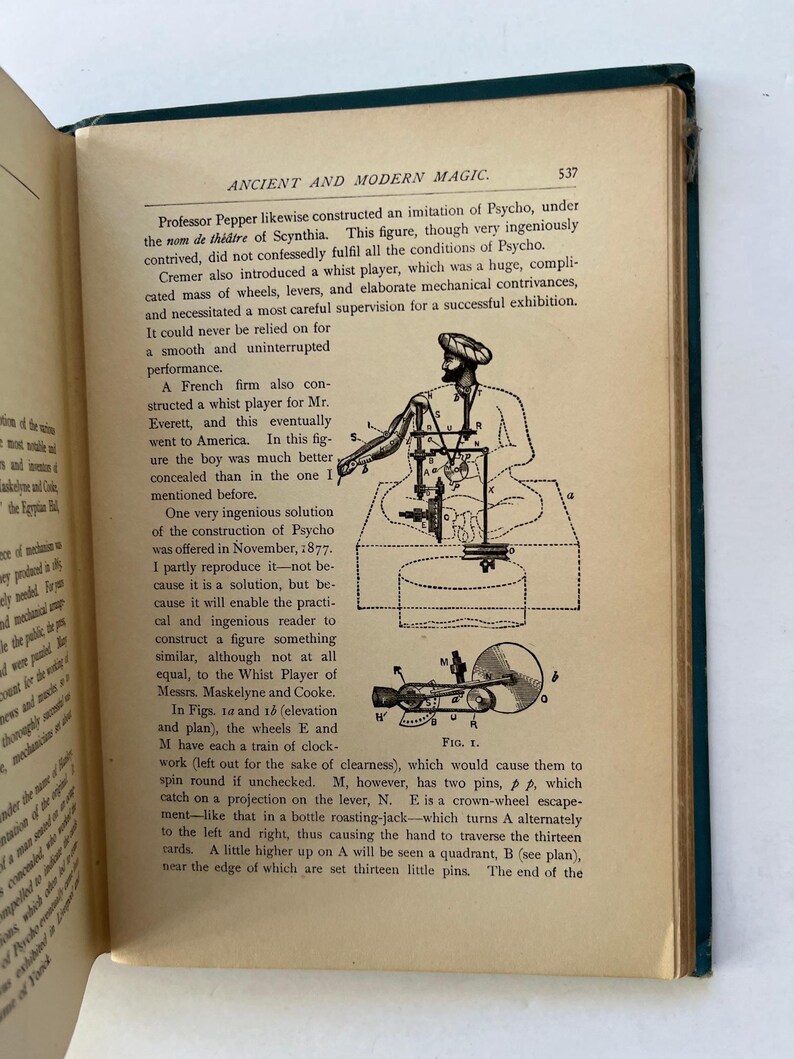 K&ouml;nnte beinhalten: Offene Buchseite mit Text und Illustrationen aus "Ancient and Modern Magic". Die Seite zeigt eine detaillierte Abbildung einer mechanischen Figur, begleitet von beschreibendem Text. Der Bucheinband ist dunkelgr&uuml;n.