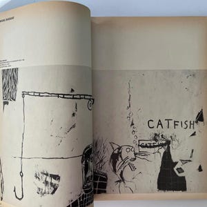 K&ouml;nnte beinhalten: Offene Buchseiten mit Schwarz-Wei&szlig;-Illustrationen. Eine Seite zeigt einen Angelhaken und abstrakte Formen. Die andere Seite zeigt das Wort "CATFISH" und eine Zeichnung einer katzenartigen Figur.