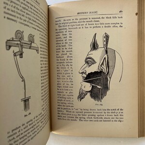 K&ouml;nnte beinhalten: Offenes Buch mit Text und Illustrationen. Die rechte Seite zeigt eine detaillierte Zeichnung einer teufelartigen Figur mit einer mechanischen Vorrichtung an ihrem Mund. Der Text lautet "MODERN MAGIC."