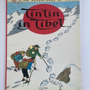 May include: A vintage copy of "The Adventures of Tintin in Tibet" comic book. The cover features a red circle with the title in white script, and illustrations of snowy mountains, footprints, and cartoon characters. Published by Little, Brown.