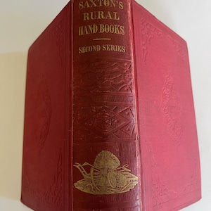 Puede incluir: Un libro rojo vintage titulado "Saxton's Rural Hand Books, Second Series". La columna vertebral presenta letras doradas y una ilustración dorada de una escena de granja. La portada tiene elementos decorativos en relieve.