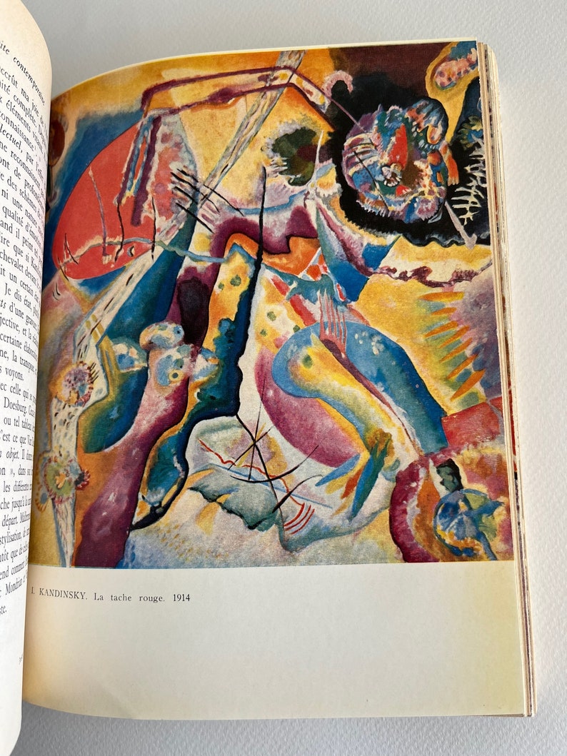 Pode incluir: Uma pintura abstrata com um esquema de cores vermelho, amarelo, azul e roxo. A pintura &eacute; intitulada "La tache rouge" e &eacute; datada de 1914. O nome do artista, "KANDINSKY", est&aacute; impresso abaixo do t&iacute;tulo.