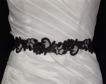 May include: A black lace bridal sash with beaded embellishments. The sash is designed with floral motifs and is perfect for adding a touch of elegance to a wedding dress.