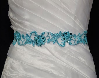 May include: A white satin wedding dress with a turquoise beaded and lace sash.