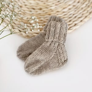 Könnte beinhalten: Ein Paar beige gestrickte Babysocken mit geripptem Bündchen.