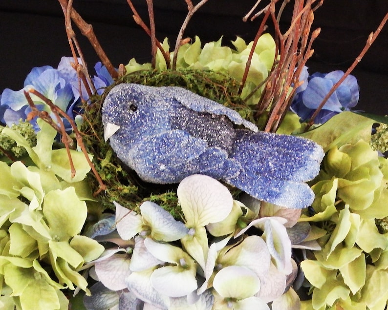 Floral arrangement with blue bird nest blue and green theme with old time wire basket large lettuce leaves floral hydrangea basket