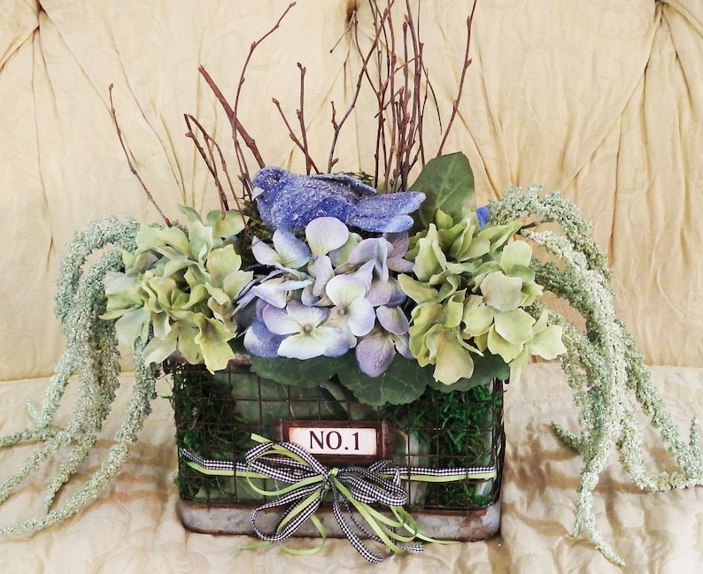 Floral arrangement with blue bird nest blue and green theme with old time wire basket large lettuce leaves floral hydrangea basket