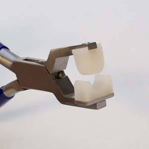 May include: Close-up of a pair of pliers with blue handles and white plastic jaws. The jaws are open and the pliers are ready to crimp.
