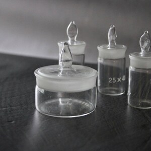 May include: Four clear glass bottles with glass stoppers. The bottles have a frosted glass top and are labelled with the text "25 x 4" and "04/12".