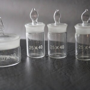 May include: Four clear glass bottles with frosted glass lids and stoppers. The bottles are labelled with the dimensions "25 x 40" and "30 x 30".