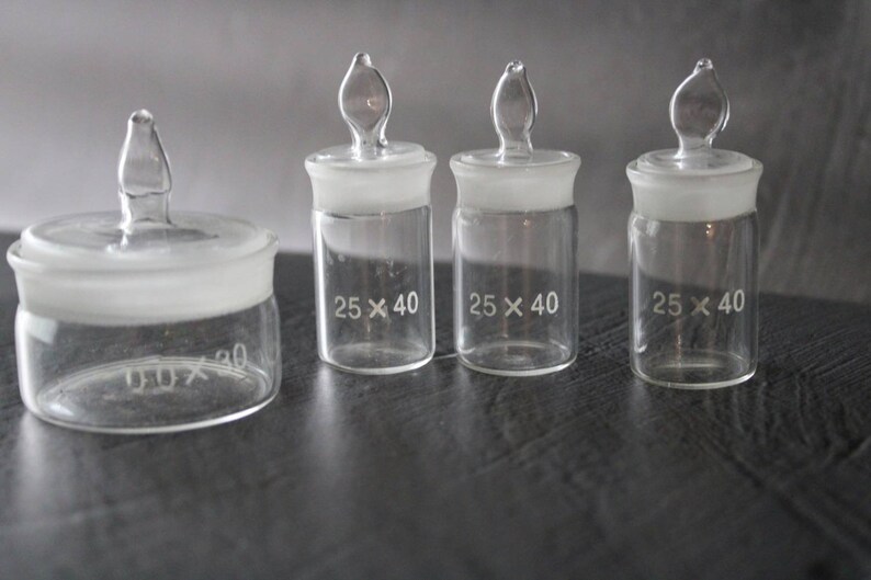 May include: Four clear glass bottles with frosted glass lids and stoppers. The bottles are labelled with the dimensions "25 x 40" and "30 x 30".