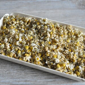May include: A white rectangular tray filled with dried chamomile flowers. The flowers are a pale yellow colour with white petals.