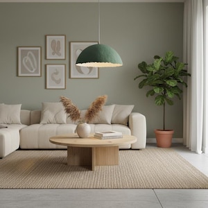 May include: A modern living room with a light beige sectional sofa, a round wooden coffee table, and a woven rug. A green pendant light hangs above the table. Artwork and a potted plant add to the room's decor.