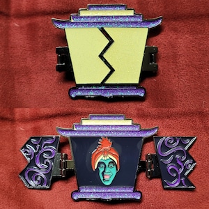 May include: A purple and gold glitter enamel pin featuring a closed and open lantern with a green face inside. The lantern has a purple and gold glitter design and a black outline. The face is green with a red turban and a white beard.