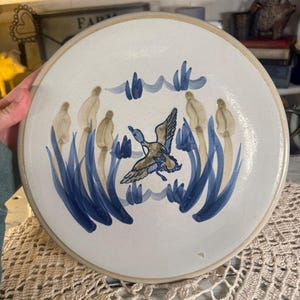 May include: A white ceramic mug with a black handle and the text "But First, Coffee" in a black, handwritten-style font. The mug is on a white surface.