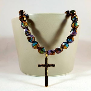 May include: A gold cross pendant necklace with iridescent brown, purple, and blue glass beads.