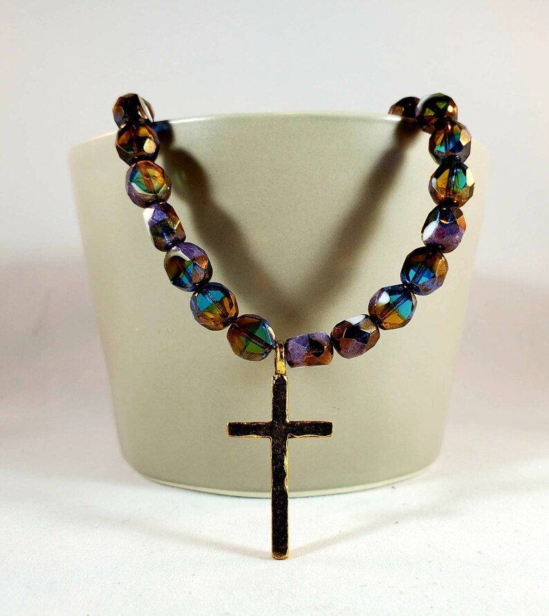 May include: A gold cross pendant necklace with iridescent brown, purple, and blue glass beads.