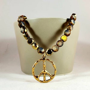 May include: A gold peace sign charm hangs from a necklace made of iridescent brown and gold beads.