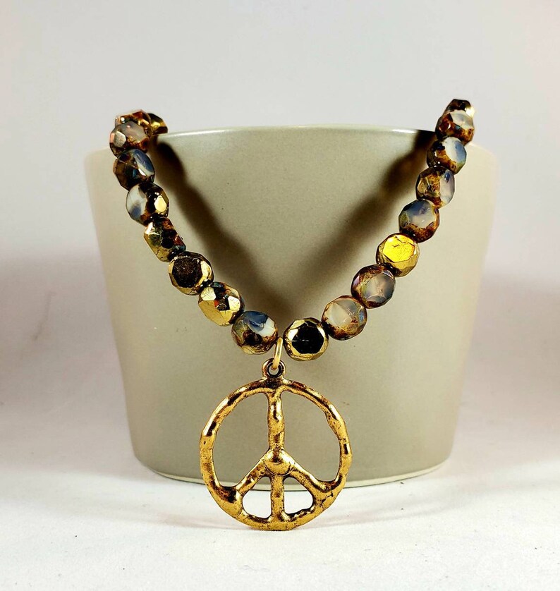 May include: A gold peace sign charm hangs from a necklace made of iridescent brown and gold beads.
